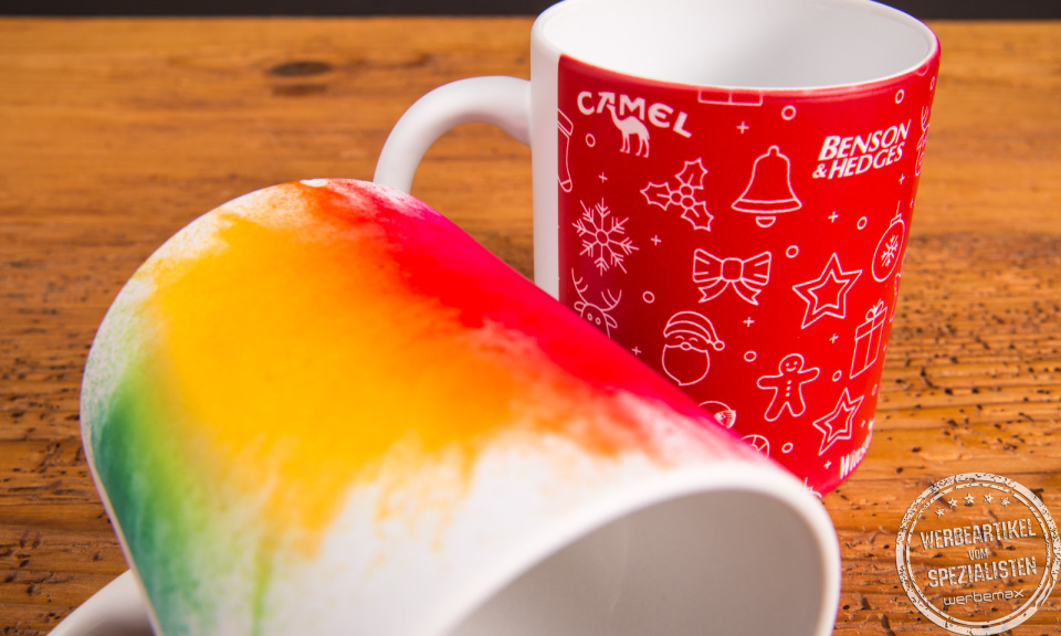 Nahaufnahme von zwei vollflächig bedruckten Werbetassen mit Regenbogenverlauf und Weihnachtsmotiv – kreative Werbeartikel Tassen von werbemax.