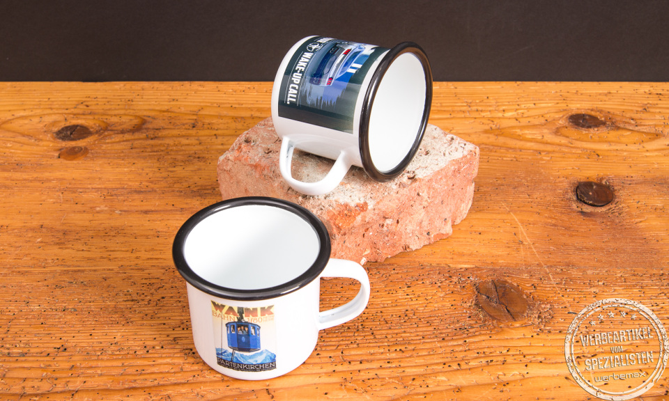 Zwei Emaille-Tassen mit Sublimationsdruck als individuelle Werbeartikel auf rustikalem Holztisch &ndash; Retro-Tassen von werbemax aus emailliertem Stahl.