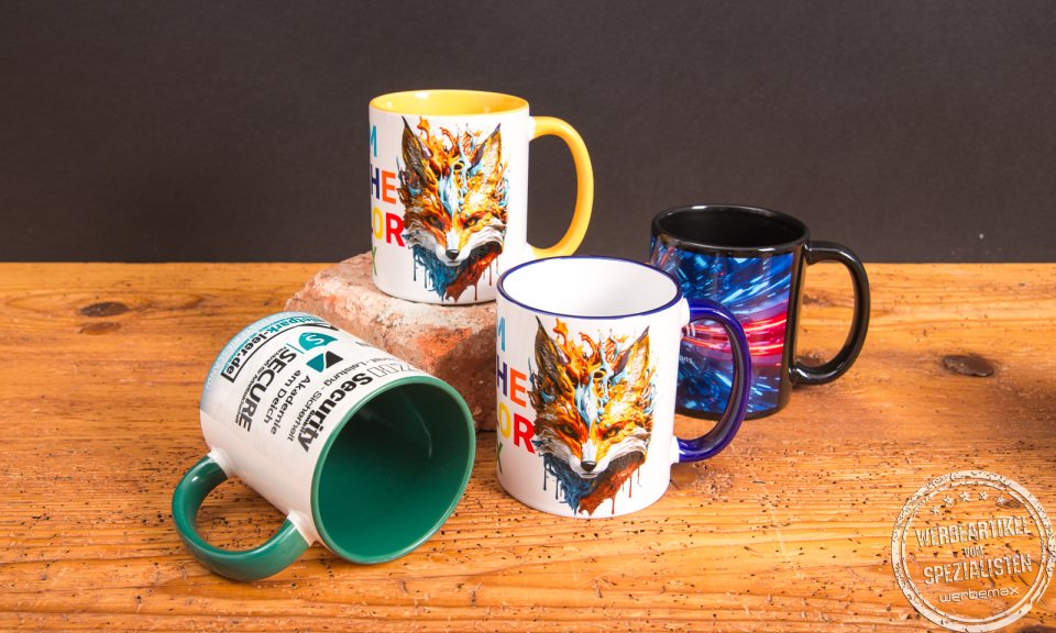Vier individuell bedruckte Keramik-Tassen mit farbigem Henkel und Innenfarbe als moderne Werbeartikel auf Holztisch &ndash; Werbetassen von werbemax f&uuml;r den B&uuml;roeinsatz.