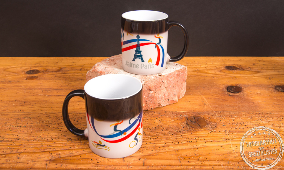 Zwei Magic-Tassen mit Farbwechsel und individuellem Aufdruck &ndash; Werbeartikel Tassen mit Thermoeffekt von werbemax auf Holztisch und Backstein platziert.