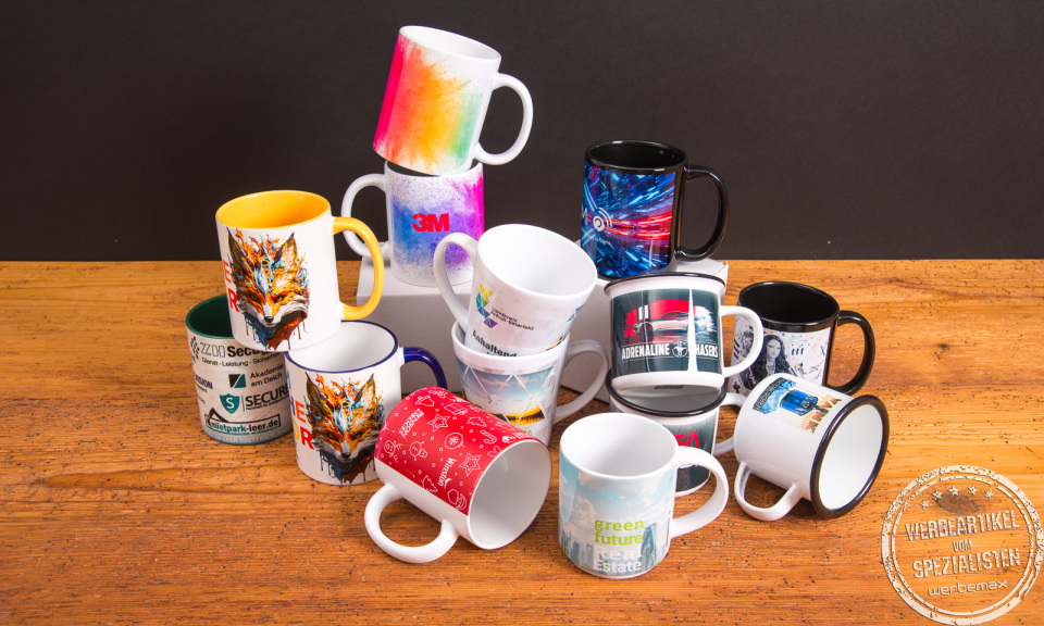 Bunte Tassen mit individuellen Fotomotiven und Logos als kreative Werbeartikel – bedruckte Kaffeebecher von Werbemax auf einem Holztisch arrangiert.