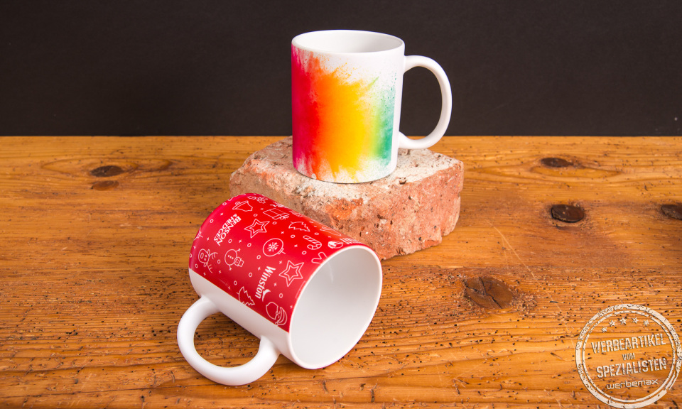 Zwei individuell bedruckte Tassen mit weihnachtlichem Design und Regenbogenverlauf &ndash; farbintensive Werbeartikel Tassen auf rustikalem Holzuntergrund.