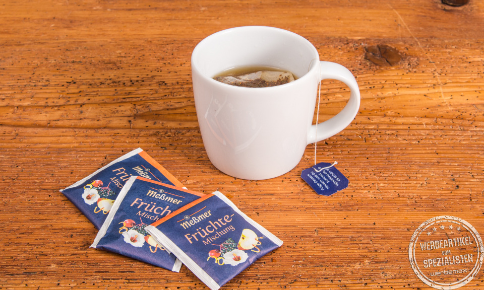 SND Porzellanbecher mit Fr&uuml;chtetee von Me&szlig;mer, Teebeutel und Verpackung daneben &ndash; perfekter Werbebecher.