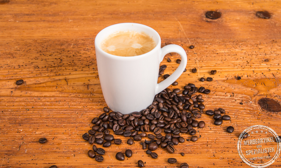 Weißer Porzellanbecher von SND mit frischem Kaffee und Kaffeebohnen – hochwertiger Werbeartikel.