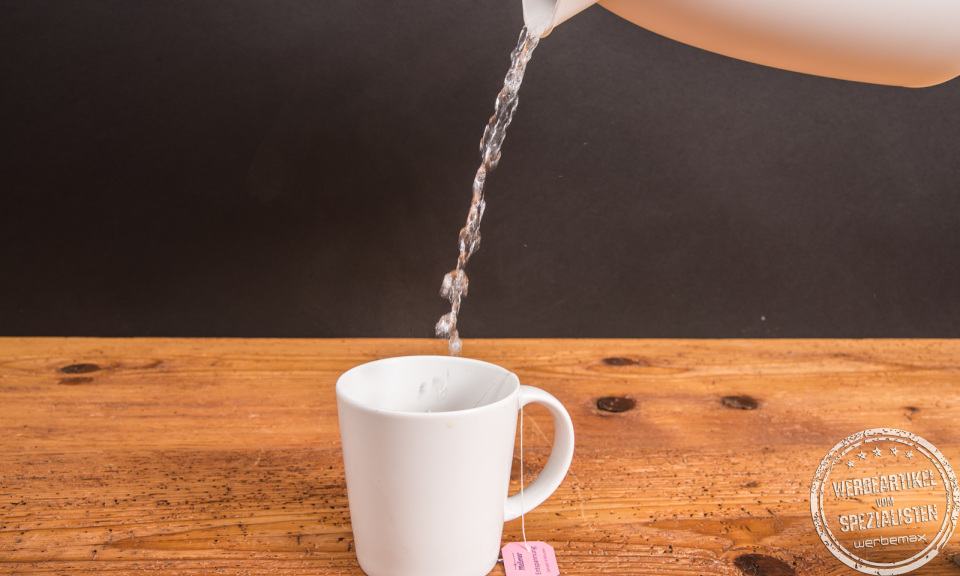 Wei&szlig;er Einfach Becher aus Porzellan von SND mit Teebeutel, wird mit hei&szlig;em Wasser aufgef&uuml;llt.