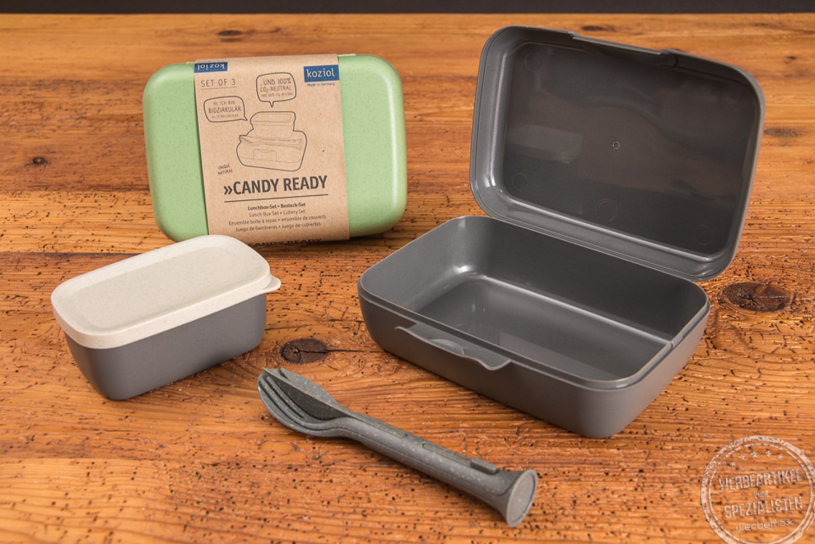 Ein geöffnetes graues koziol Candy Ready Lunchbox Set inklusive Besteck und kleiner auslaufsicheren Dose, sowie eine geschlossene grüne Candy-Ready Lunchbox. 