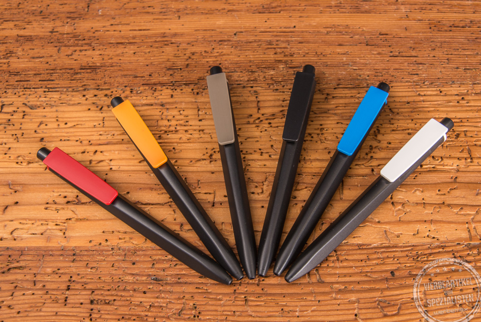 Sechs Ritter Pen Kugelschreiber Ridge Recycelt in schwarz mit unterschiedlichen Schaftfarben liegend auf Holzfläche. 