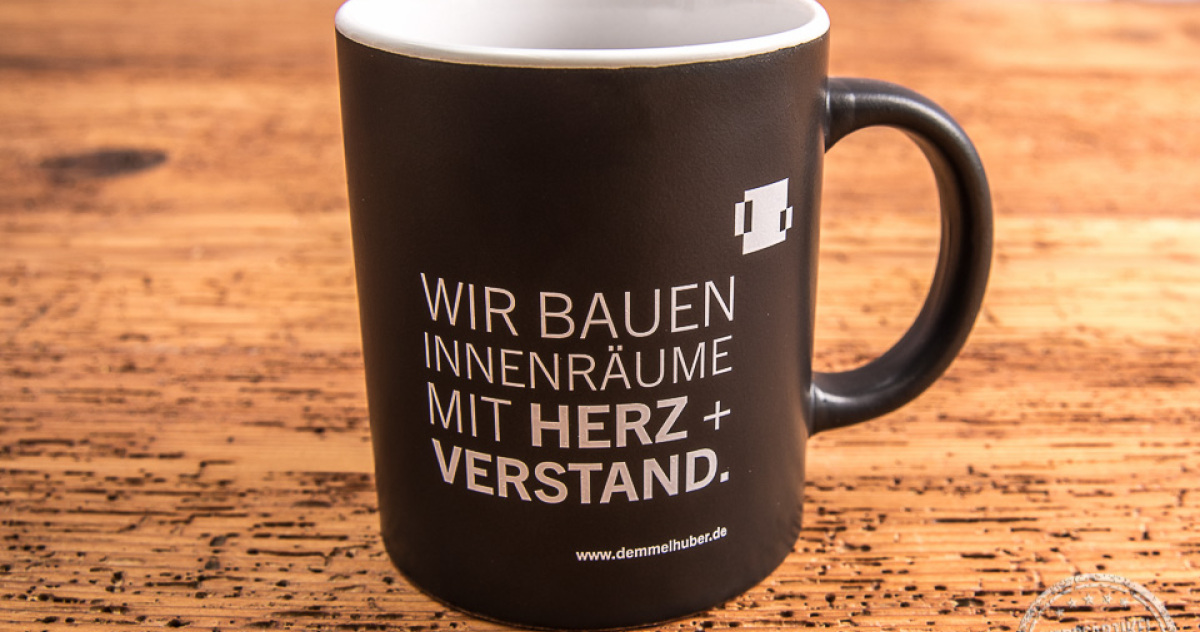 Schwarze Tasse mit weißer Werbeanbringung von Baierl + Demmelhuber