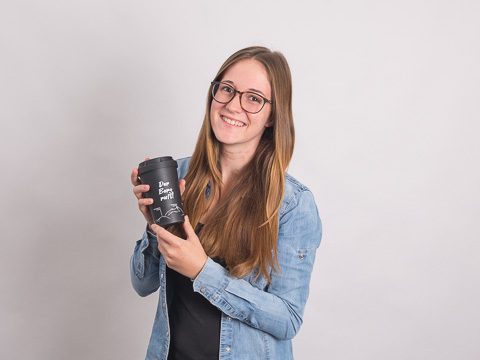 Melanie Brenner, werbemax Kundenberaterin mit einem Kaffeebecher to go als Werbegeschenk in der Hand. 