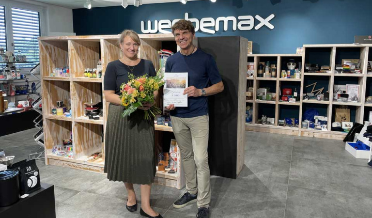 Irina Belger mit Blumenstrauß in der Hand zusammen mit Gerhard Betzold im werbemax Showroom anlässlich Irinas Firmenjubiläum.