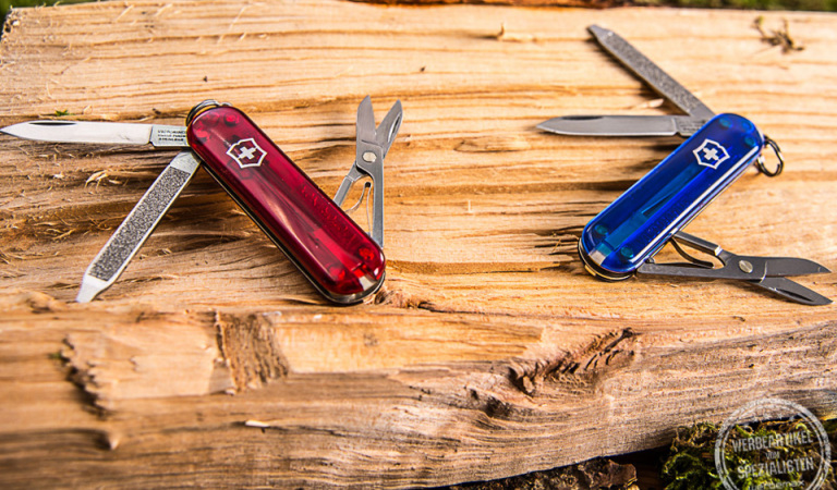 Zwei Victorinox Taschenmesser Classic SD aufgeklappt auf Holz liegend als Werbeartikel.