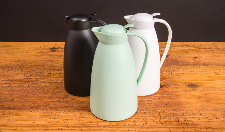 Drei alfi Isolierkannen ECO in Schwarz, Wei&szlig; und Mintgr&uuml;n auf Holztisch &ndash; stilvolle Thermoskannen als nachhaltige Werbeartikel mit Logo.