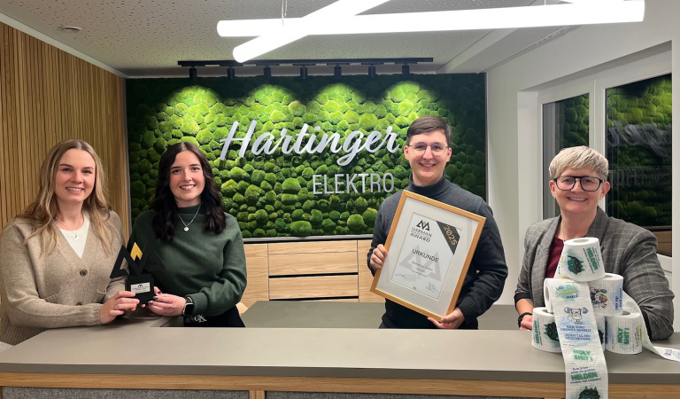 Team von Elektro Hartinger mit dem German Marketing Award 2025, der prämierten Urkunde und dem kreativen Werbemittel bedrucktes Toilettenpapier, entwickelt von werbemax.