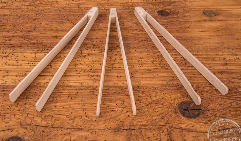 Drei Grillzangen aus Buchenholz als Werbegeschenk liegen nebeneinander auf einer Holztischplatte