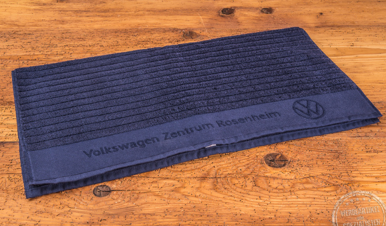 Kundenreferenz blaues Badetuch VW-Zentrum als hochwertiges Kundengeschenk auf Holzboden