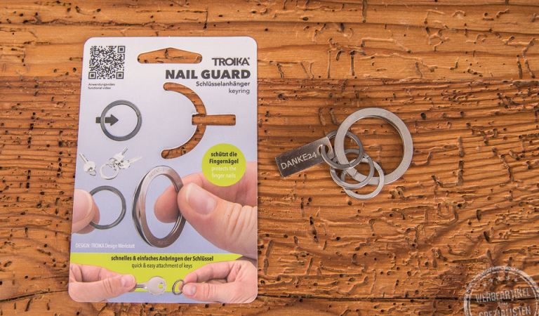 Troika Schlüsselanhänger Nail Guard liegend neben der Verpackung als Werbeartikel.
