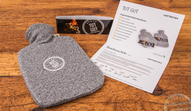 Wärmflasche als Werbegeschenk für Kunden in Mailingaktion mit offener Karte auf Holztisch