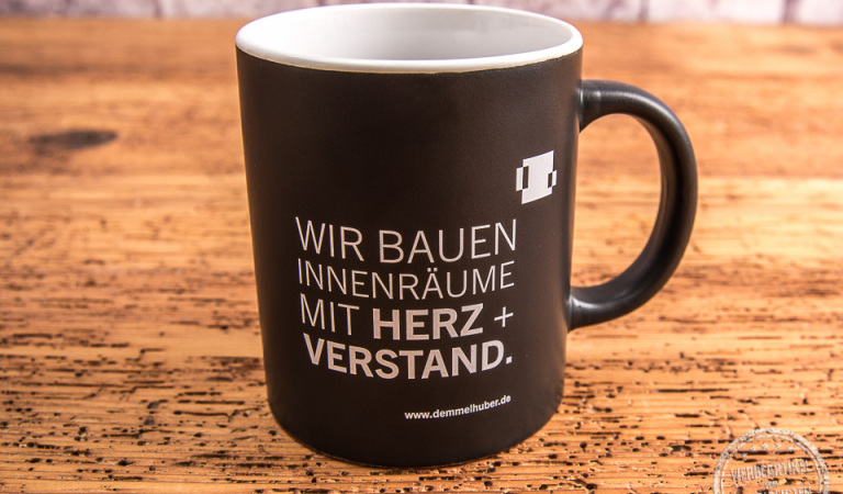 Schwarze Tasse mit weißer Werbeanbringung von Baierl + Demmelhuber