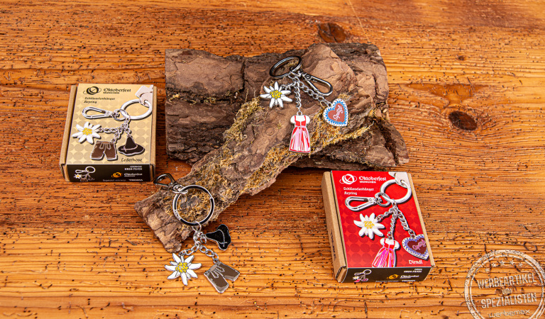 Zwei Oktoberfest Schlüsselanhänger der Marke TROIKA mit den Motiven Dirndl und Lederhose.