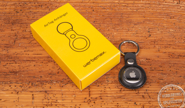 Apple AirTag mit edlem schwarzen Schlüsselanhänger als hochwertiges Werbegeschenk auf Holztisch – praktische Geschenkidee mit Logo für Kunden oder Mitarbeiter, ideal zum Wiederfinden von Schlüsseln und Taschen.