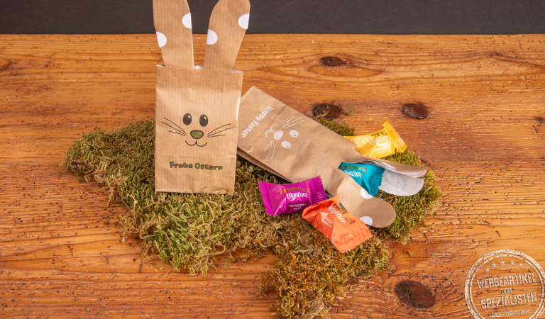 Ostertüte Bunny Bag mit Süßigkeiten von Merci als Werbegeschenk im Moos auf Holztischplatte..