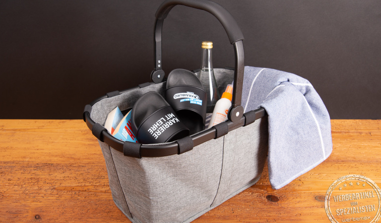 Reisenthel Carrybag Twist Silver in Grau, befüllt mit Sommerutensilien wie Handtuch, Sandalen und Getränk – stilvoller Einkaufskorb als hochwertiges Werbegeschenk oder Mitarbeiterpräsent.