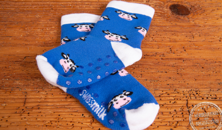 Blaue Babysocken mit Anti-Rutsch-Noppen und Einwebungen eines Kuhmotives. Die Babysocken liegen auf einem Holztisch.