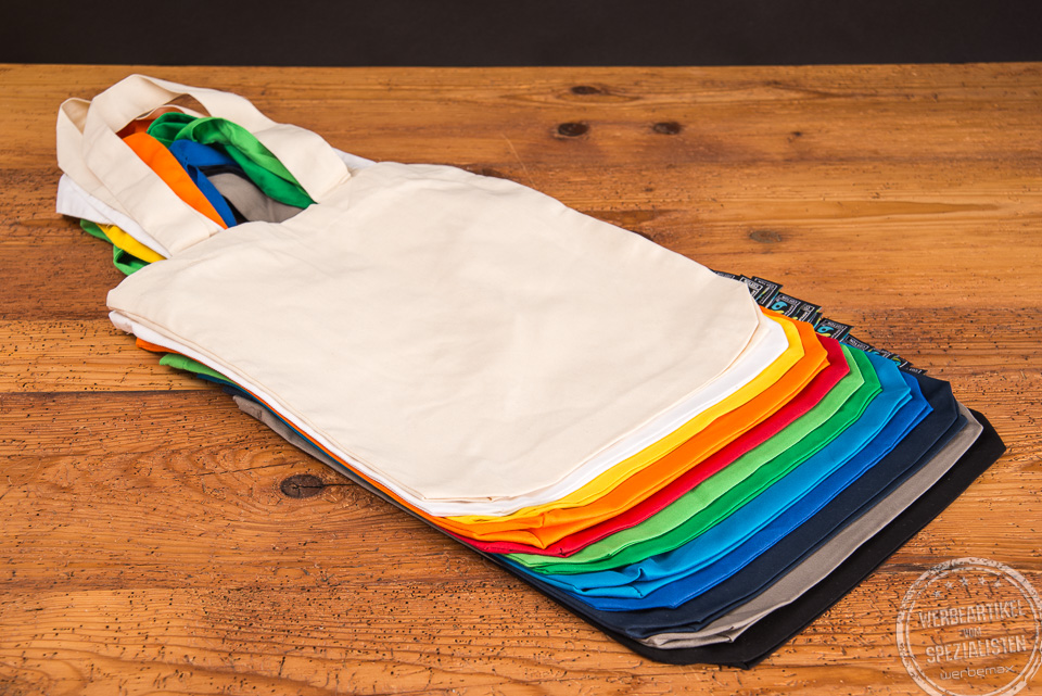 Hochwertige Messetasche mit Bodenfalten aufgef&auml;chert um die gro&szlig;e Farbvielfalt besser zu sehen auf Holztisch &uuml;bereinander liegend.