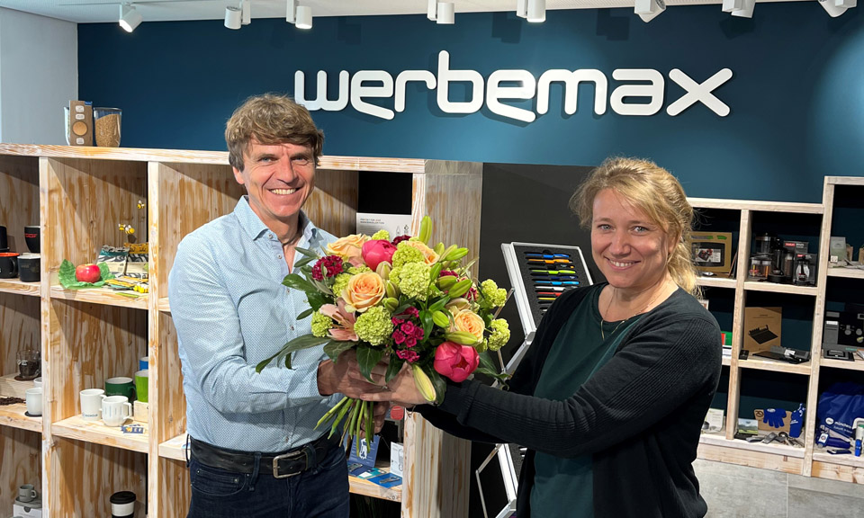 Gerhard Bezold Gesch&auml;ftsf&uuml;hrer werbemax erteilt Prokura Irina Belger im werbemax Showroom mit Blumenstrau&szlig;